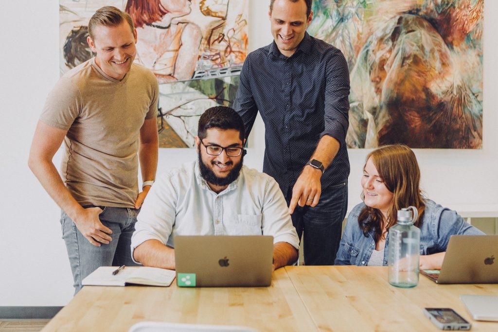 4 people looking at laptop, 2 standing, 2 sitting